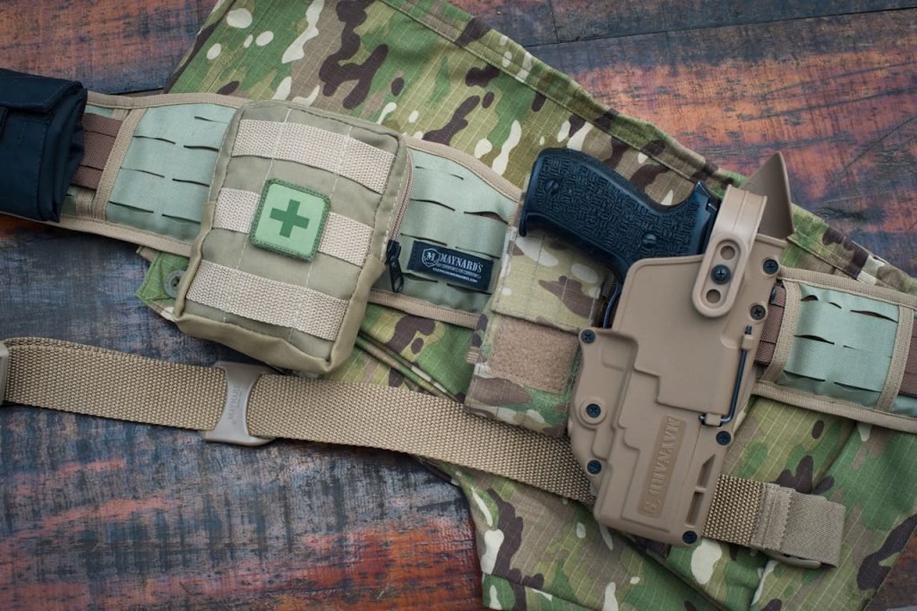 Top view of military gear with gun holster and tactical belt on camouflage fabric.