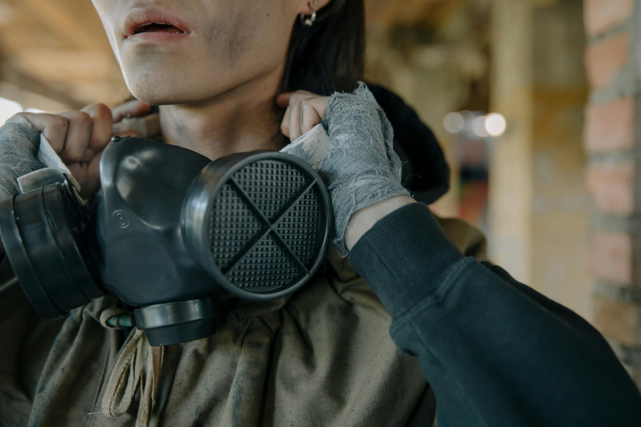 A person with a gas mask and bandaged hands in an urban setting, indicating survival theme.