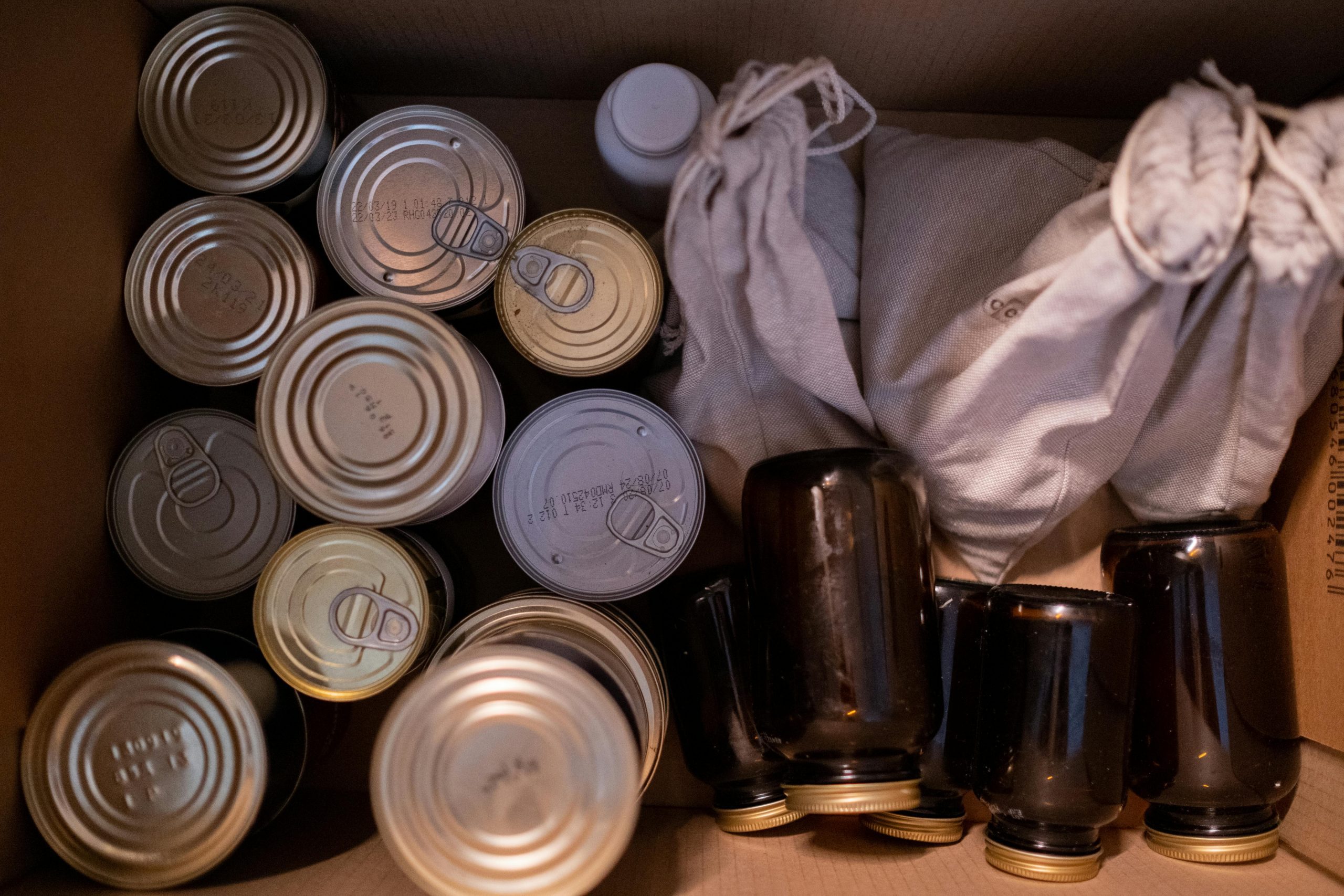 Top view of a box filled with canned goods, jars, and cloth sacks for storage.