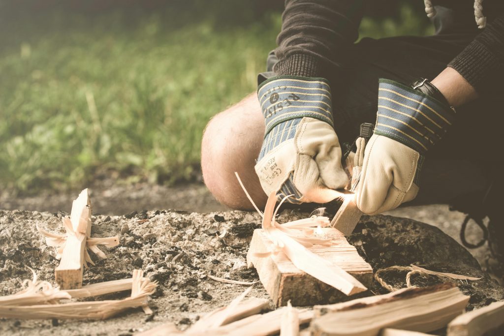 A person using a firestarter to ignite wood shavings, demonstrating bushcraft skills in a natural setting.